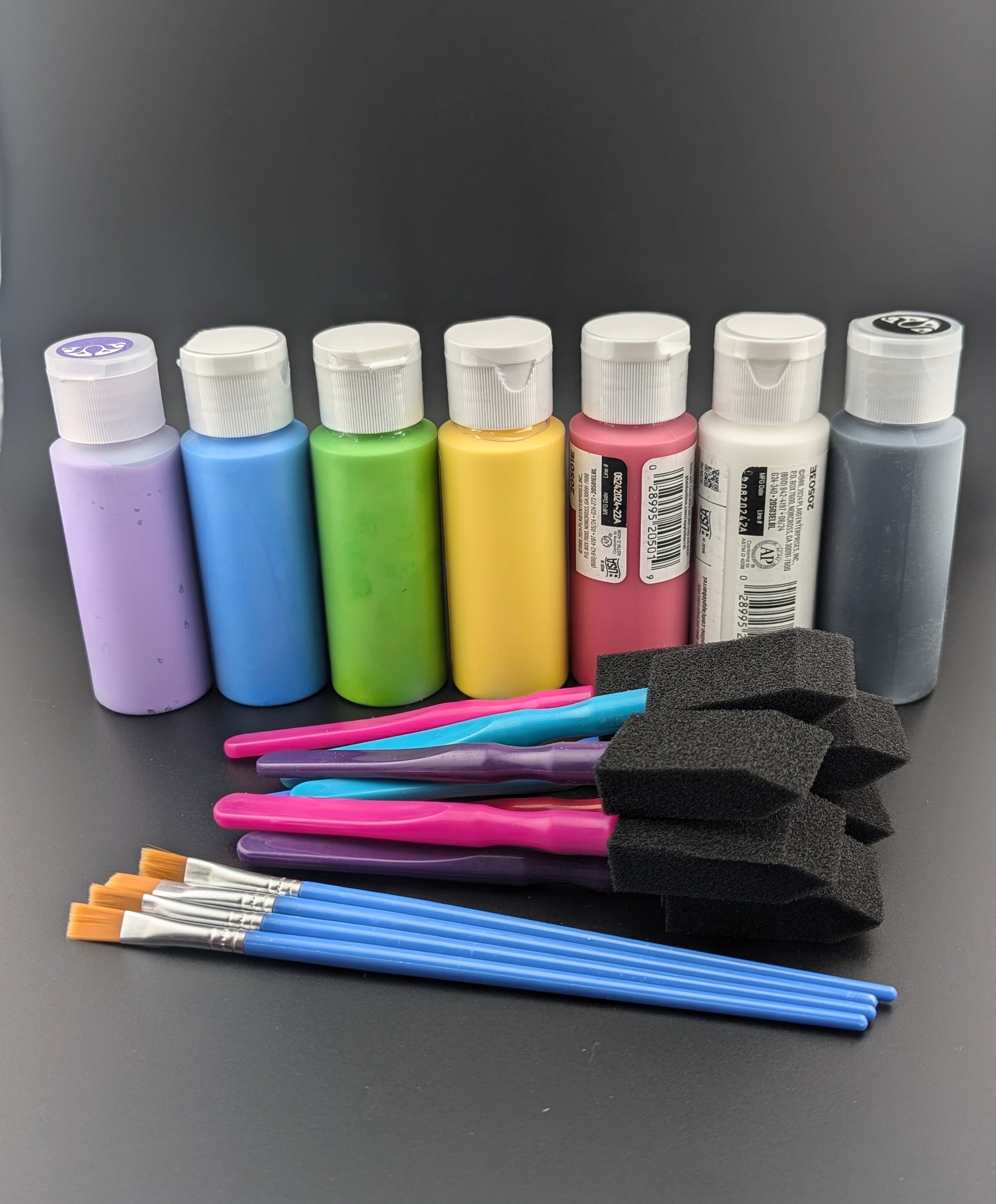 A line of 8 paint bottles with foam brushes on a black backdrop.